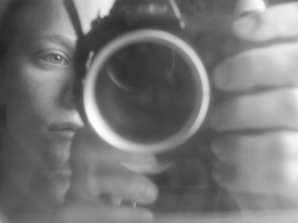 Black and white close-up of an eye reflected in a camera lens — the photographer’s point of view